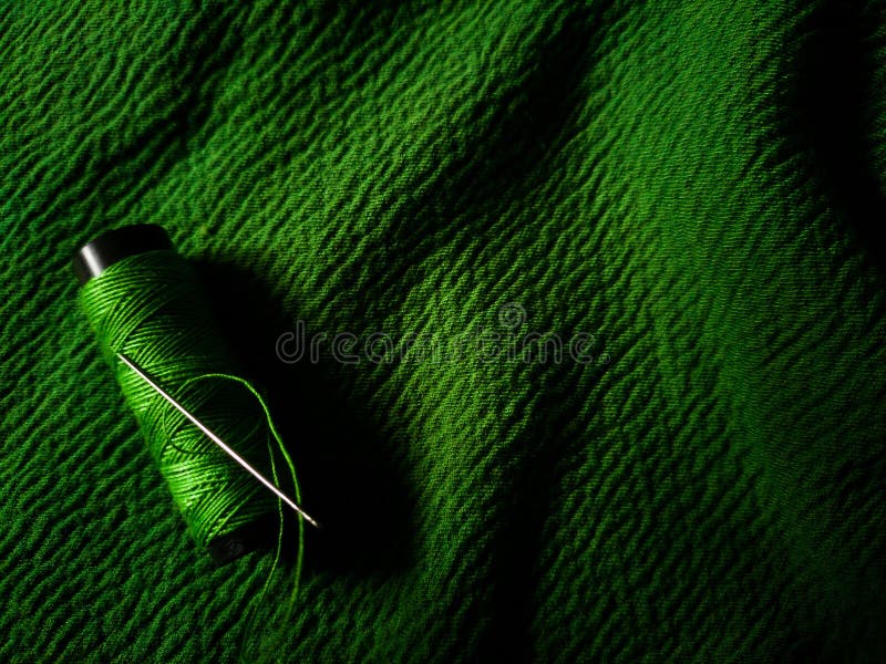 Green thread spool lies on a green textured fabric stock images