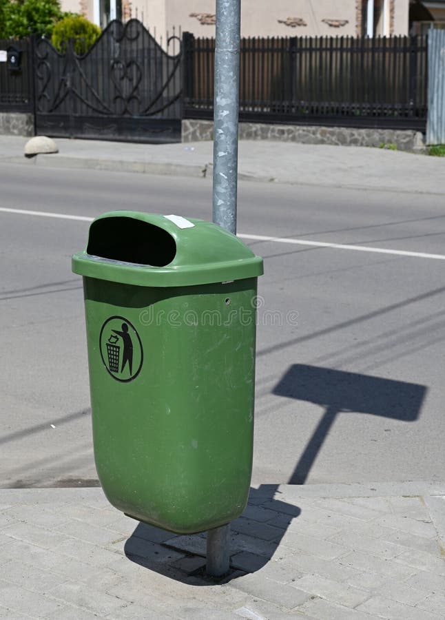 Green trash bin attached to a metal pole on a city sidewalk during bright daylight stock image