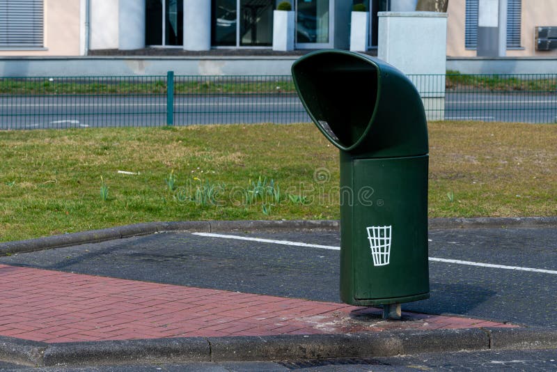 Green trash bin in urban area near grass and pavement stock photo