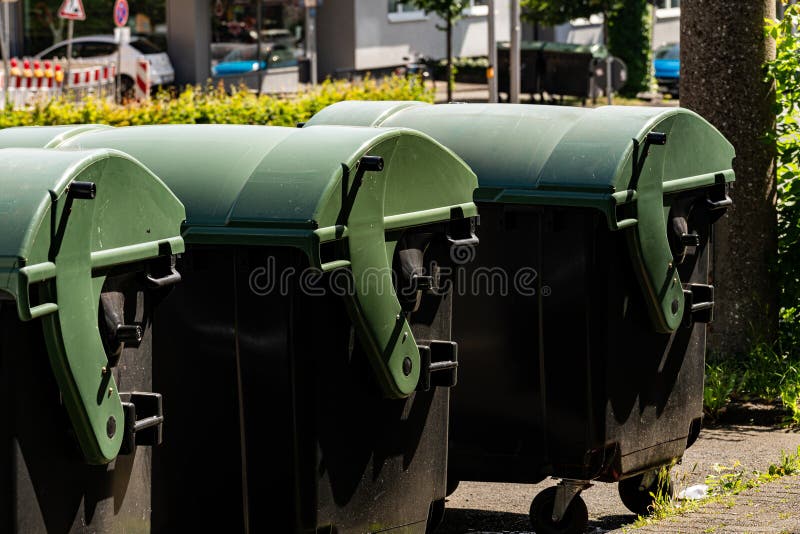 Green trash bins lined up along a city sidewalk in daylight stock photos