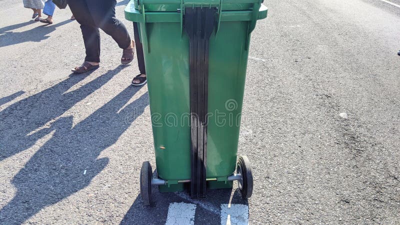 A green trash can with wheels on a paved road. royalty free stock images