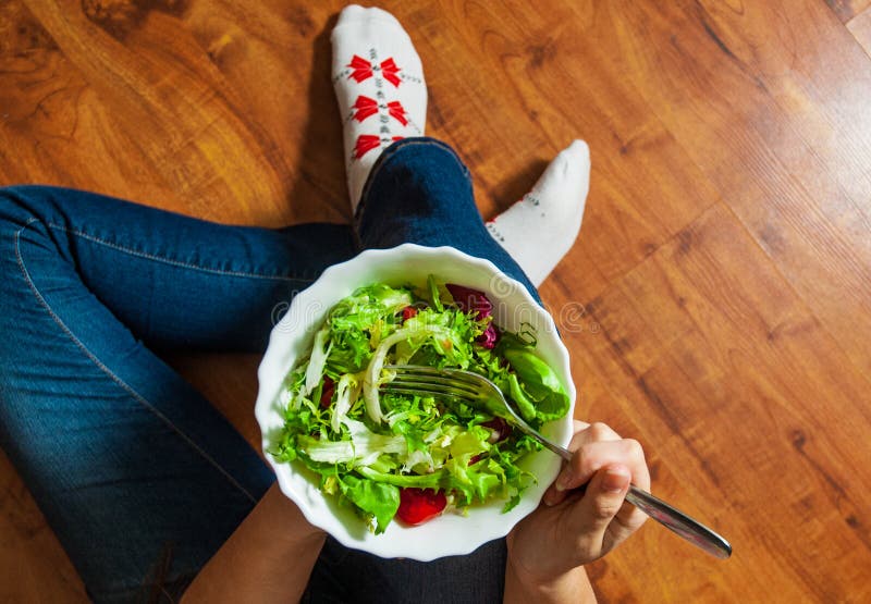 Vegan breakfast meal in bowl with various fresh mix salad leaves and tomato. Girl in jeans holding fork with knees and hands visib