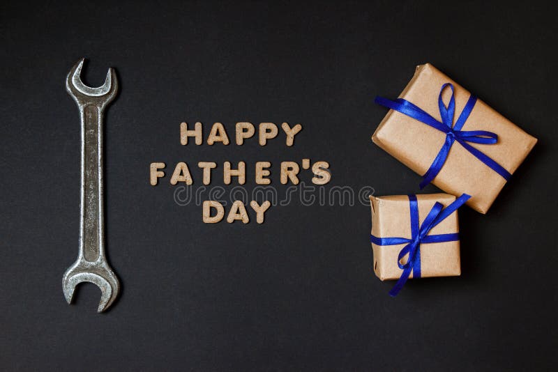 Greeting card to celebrate Father`s day. Two craft gifts with blue ribbons with tool on paper black background royalty free stock images Greeting card to celebrate Father`s day. Two craft gifts with blue ribbons with tool on paper black background royalty free stock images