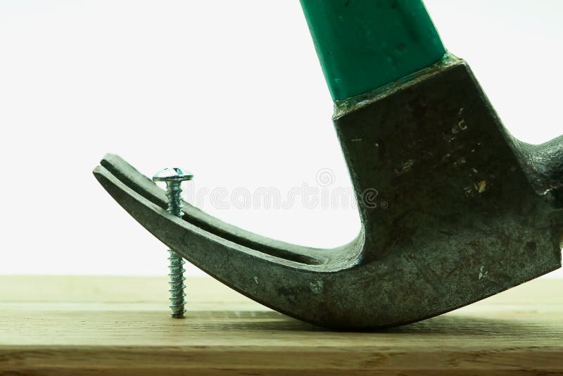 An old claw hammer with green handle is used to try in vain to remove a shiny silver colored from a wooden plank. An old claw hammer with green handle is used to try in vain to remove a shiny silver colored from a wooden plank.