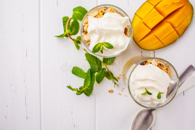 Grekisk parfait för yoghurtmangogranola i ett exponeringsglas på vita trälodisar arkivfoto Grekisk parfait för yoghurtmangogranola i ett exponeringsglas på vita trälodisar arkivfoto
