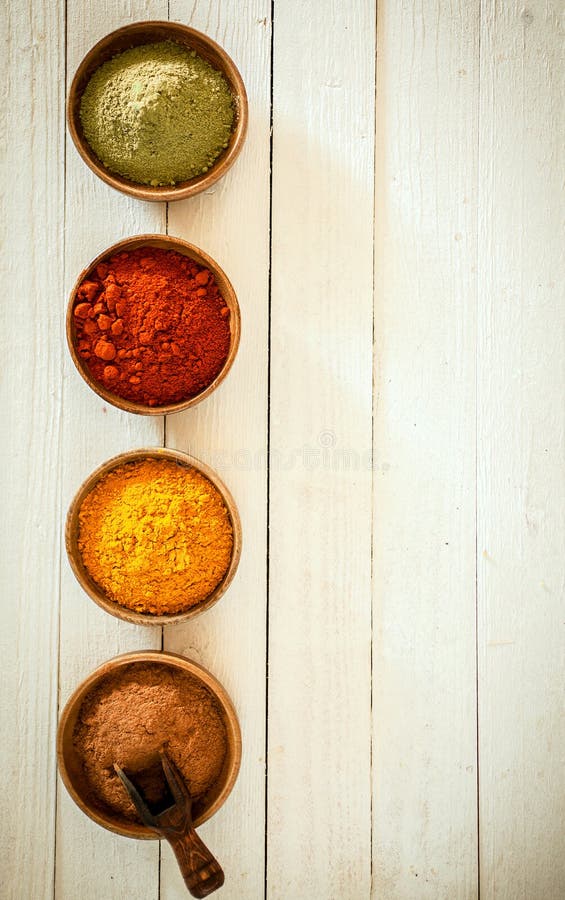 Border of colourful spices arranged in a vertical row with chilli, curry, red pepper and matcha powder in small bowls on a background of white painted boards with copyspace. Border of colourful spices arranged in a vertical row with chilli, curry, red pepper and matcha powder in small bowls on a background of white painted boards with copyspace