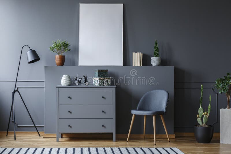 Grey cabinet between black lamp and chair in living room interior with mockup of poster. Real photo stock image