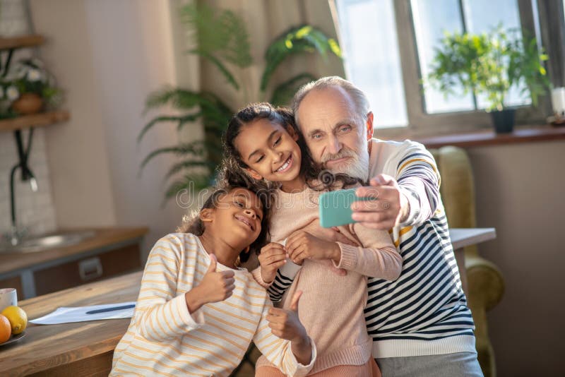 Grey-haired bearded man and his granddaughters looking happy stock photography
