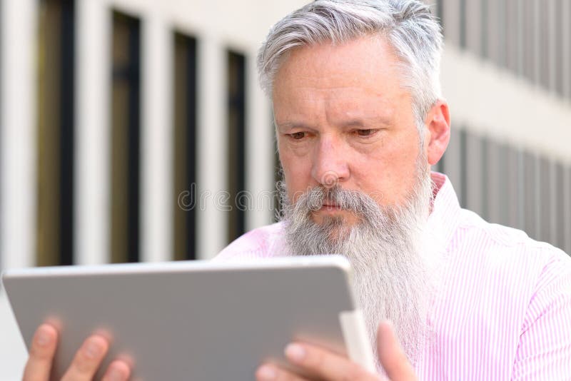 Grey-haired bearded man reading on a tablet stock photos