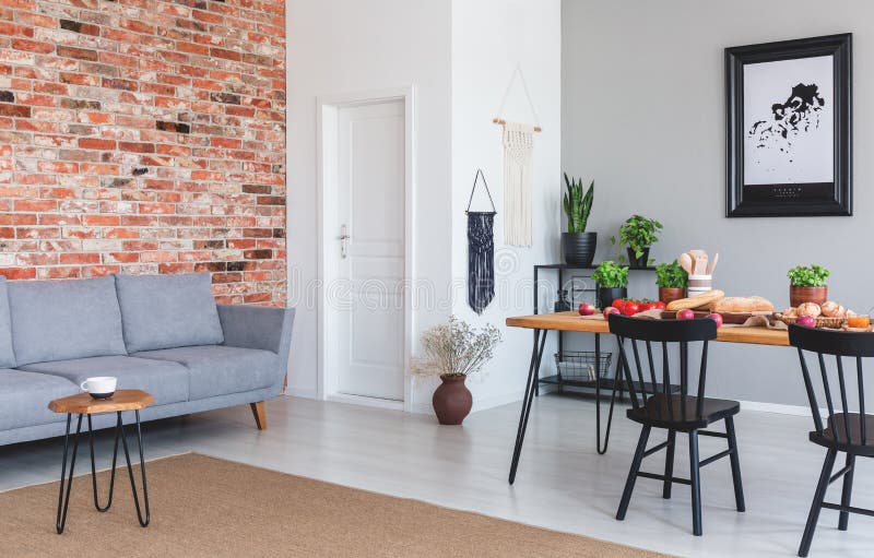 Grey sofa against red brick wall in flat interior with poster and black chairs at dining table. Real photo stock photography Grey sofa against red brick wall in flat interior with poster and black chairs at dining table. Real photo stock photography