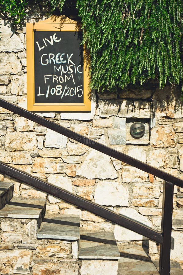 A sign for live greek music next to some stone steps. A sign for live greek music next to some stone steps