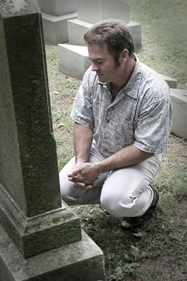 Un uomo in un cimitero con mani giunte in segno di riverenza, parzialmente desaturati.