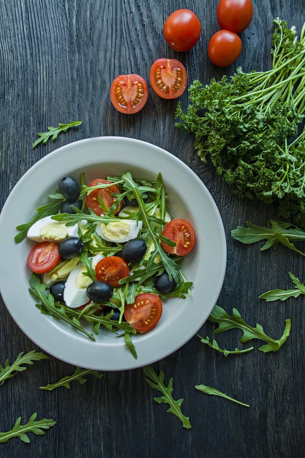 Griekse salade met verse tomaten, arugula, eieren, olijven met olijfolie op een donkere houten achtergrond Gezond voedsel Veggie stock foto's Griekse salade met verse tomaten, arugula, eieren, olijven met olijfolie op een donkere houten achtergrond Gezond voedsel Veggie stock foto's