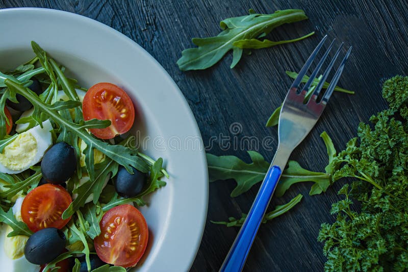 Griekse salade met verse tomaten, arugula, eieren, olijven met olijfolie op een donkere houten achtergrond Gezond voedsel Veggie stock foto Griekse salade met verse tomaten, arugula, eieren, olijven met olijfolie op een donkere houten achtergrond Gezond voedsel Veggie stock foto