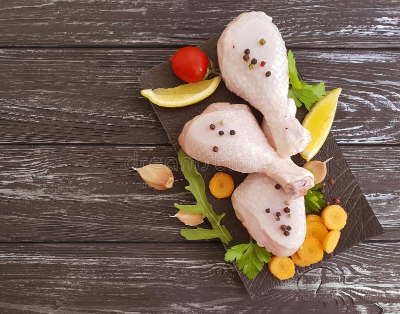 Griglia organica su un fondo del bordo di legno, carote, limone, prezzemolo, pepe dei piedi crudi del pollo immagine stock Griglia organica su un fondo del bordo di legno, carote, limone, prezzemolo, pepe dei piedi crudi del pollo immagine stock
