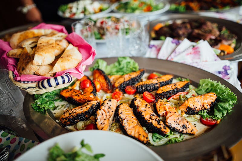 Grill crusted salmon with black sesame seeds and greens dish served on full feast dinner table.Special occasion.Healthy