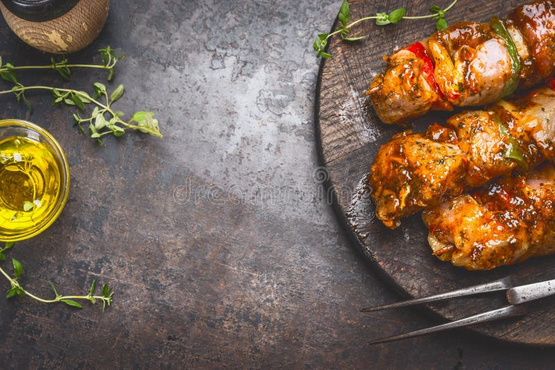 Grill food background with marinated skewers, meat fork, herbs spices and oil on dark rust metal background, top view