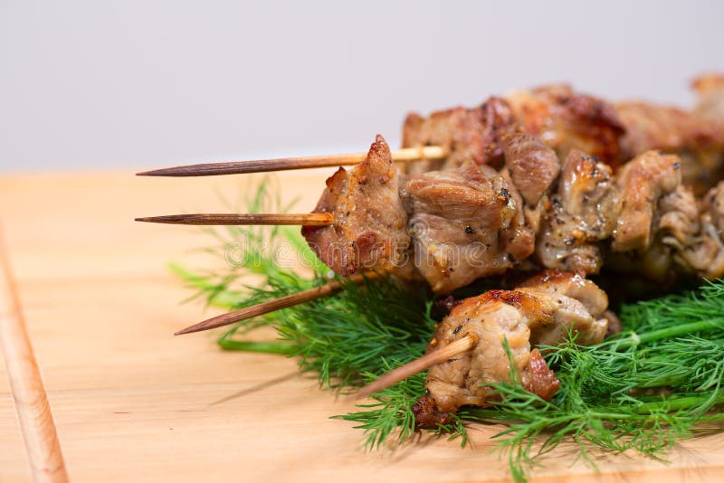 Grill meat on a sticks with green on wooden plate