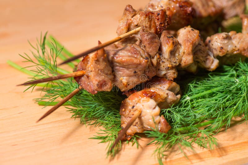 Grill meat on a sticks with green on wooden plate