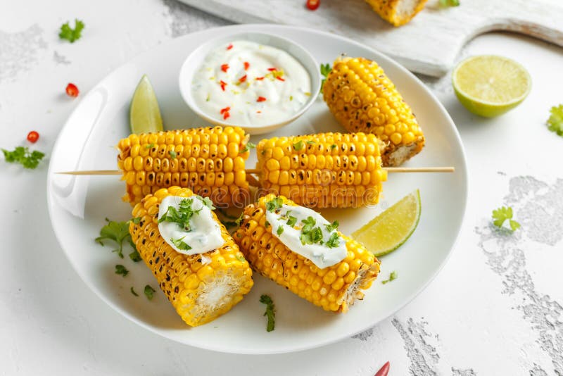 Grillad majs med den vit mexikansk sås, chili och limefrukt Sund sommarmat royaltyfri foto Grillad majs med den vit mexikansk sås, chili och limefrukt Sund sommarmat royaltyfri foto