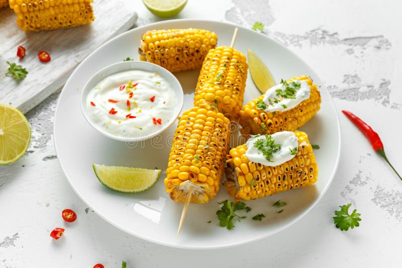 Grillad majs med den vit mexikansk sås, chili och limefrukt Sund sommarmat royaltyfri bild Grillad majs med den vit mexikansk sås, chili och limefrukt Sund sommarmat royaltyfri bild