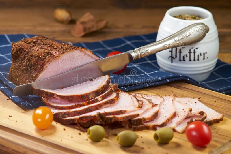 Grillad skinka, skivad ‹för ​†och konsumtionsfärdigt. Bakad skinka, snitt för några aptitretande skivor med en kniv från ett större stycke De ligger på ett konsumtionsfärdigt träbräde