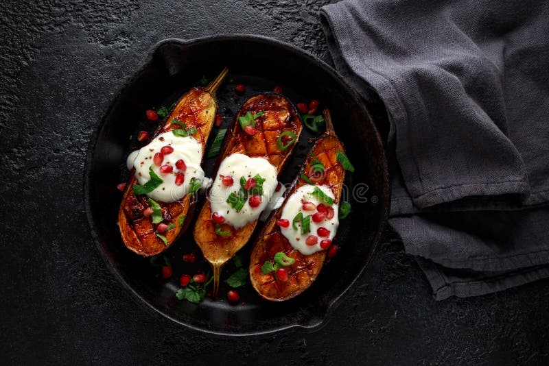Grillade aubergine med yoghurtsås, granatäpplefrö, persilja och salladslöken i gjutjärntappningpanna royaltyfria foton Grillade aubergine med yoghurtsås, granatäpplefrö, persilja och salladslöken i gjutjärntappningpanna royaltyfria foton