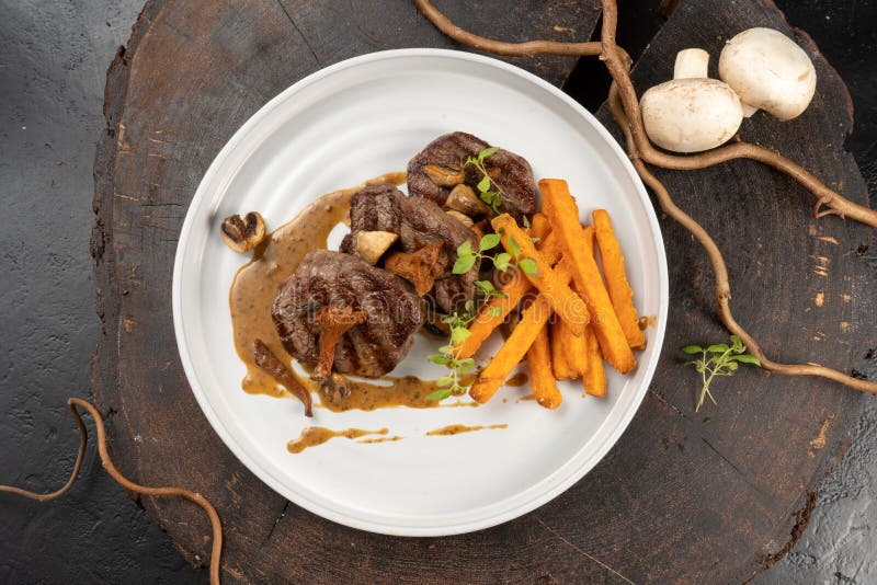 Grilled beef medallions with a side dish of sweet potatoes and mushroom sauce of mushrooms. main hot meat dish.