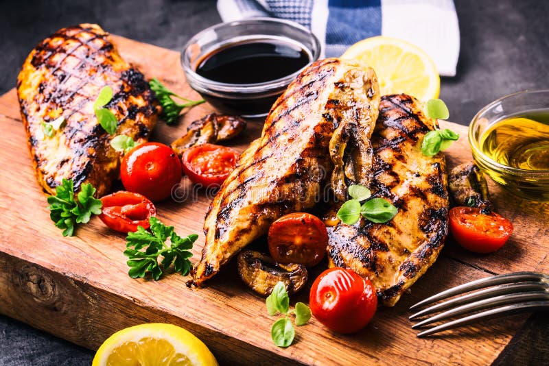 Grilled chicken breast in different variations with cherry tomatoes, mushrooms, herbs, cut lemon on a wooden board or teflon pan.