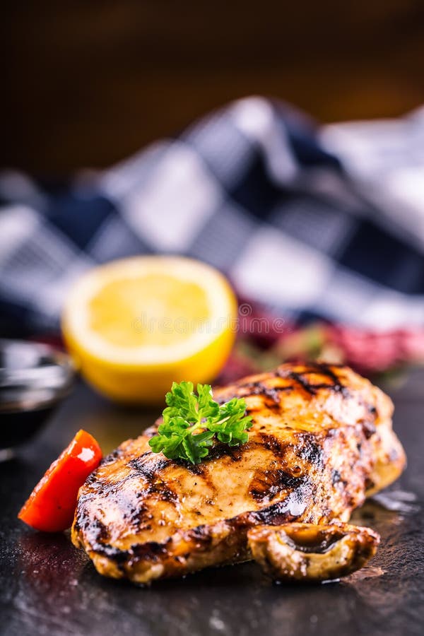 Grilled chicken breast in different variations with cherry tomatoes, mushrooms, herbs, cut lemon on a wooden board or teflon pan.