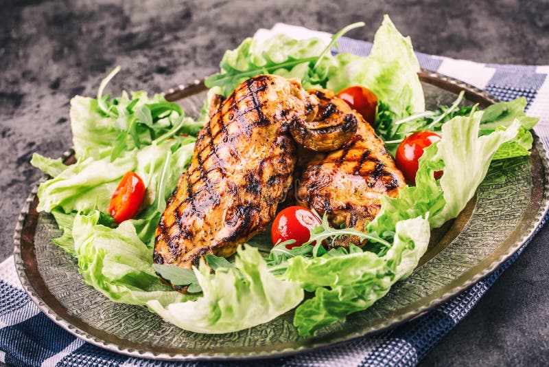 Grilled chicken breast in different variations with lettuce salad cherry tomatoes mushrooms herbs cut lemon on a wooden board or