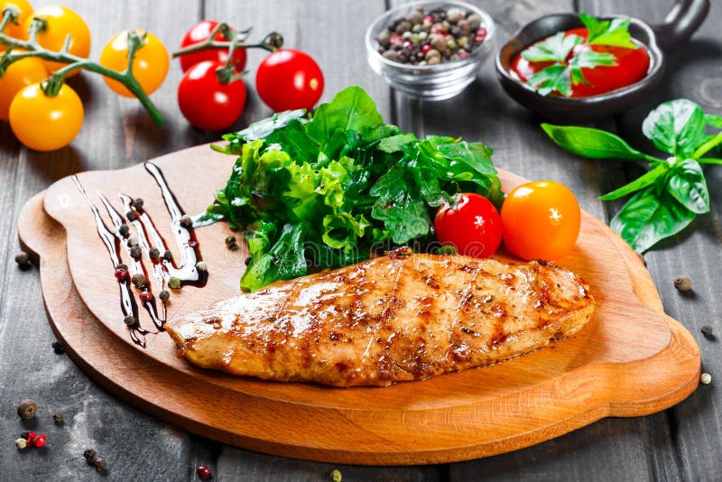 Grilled chicken fillet with fresh vegetable salad, tomatoes and sauce on wooden cutting board.