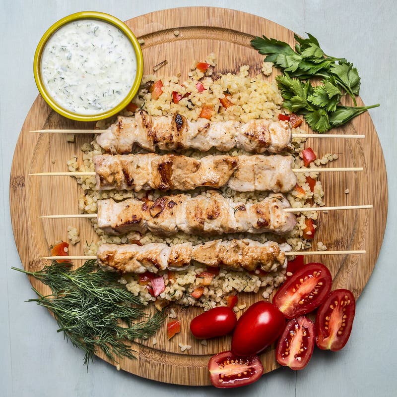 Grilled chicken on skewers with garlic sauce and bulgur dill parsley and tomatoes on a cutting board wooden background top view stock images Grilled chicken on skewers with garlic sauce and bulgur dill parsley and tomatoes on a cutting board wooden background top view stock images