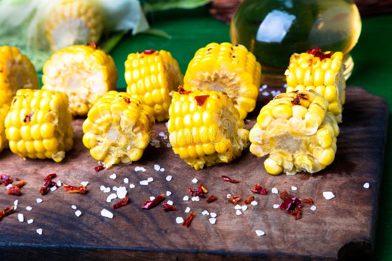 Grilled corn slices on wooden board with salt and red dried pepper. Close up.