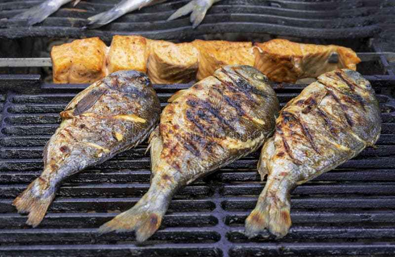 Grilled Dorada Fish and Slices of Salmon on the Grill Grate Stock Photo