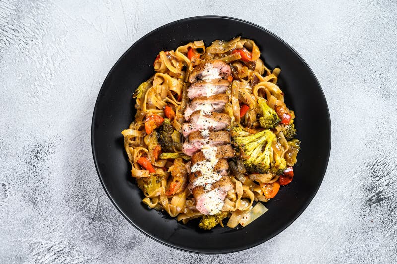 Grilled duck breast with Udon noodles and vegetables. Gray background. Top view