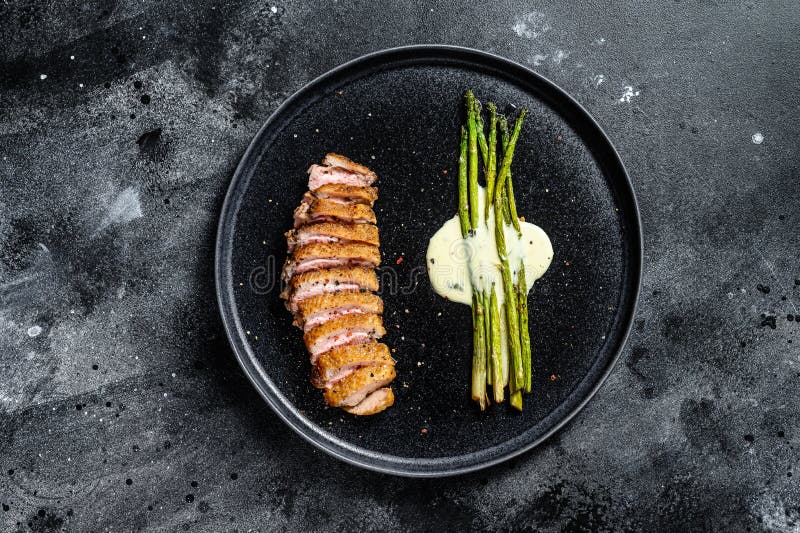 Grilled Duck fillet steaks with asparagus. Black background. Top view