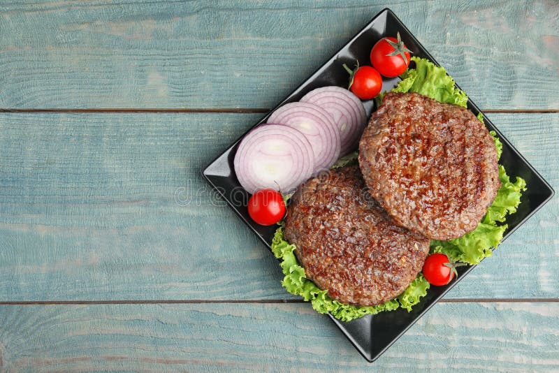 Grilled meat cutlets for burger on blue wooden table. Space for text