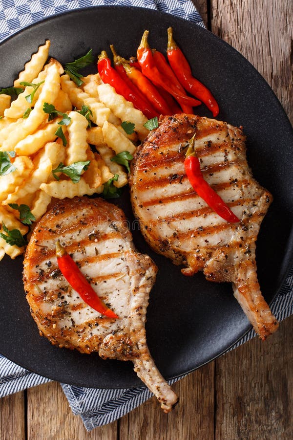 Grilled pork with bone, chili and fries close-up on plate. Verti