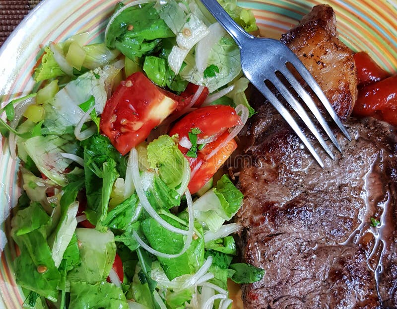 Grilled Ribeye beef steak with a large portion of fresh salad on a color plate