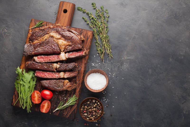 Grilled ribeye beef steak with red wine, herbs and spices on a dark stone background. Top view with copy space for your text royalty free stock photography Grilled ribeye beef steak with red wine, herbs and spices on a dark stone background. Top view with copy space for your text royalty free stock photography