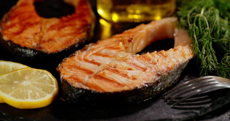 Grilled salmon steaks with lemon slices and herbs rotate.