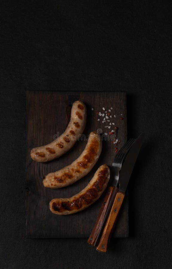 Grilled sausages on a dark wooden board top view