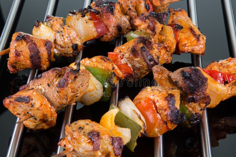 Grilled shaslik skewers on a cooking grate with reflections on a