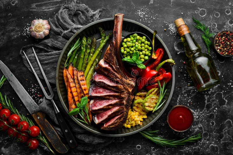 Grilled steak on the bone with grilled vegetables. On a black background. Top view. Free copy space