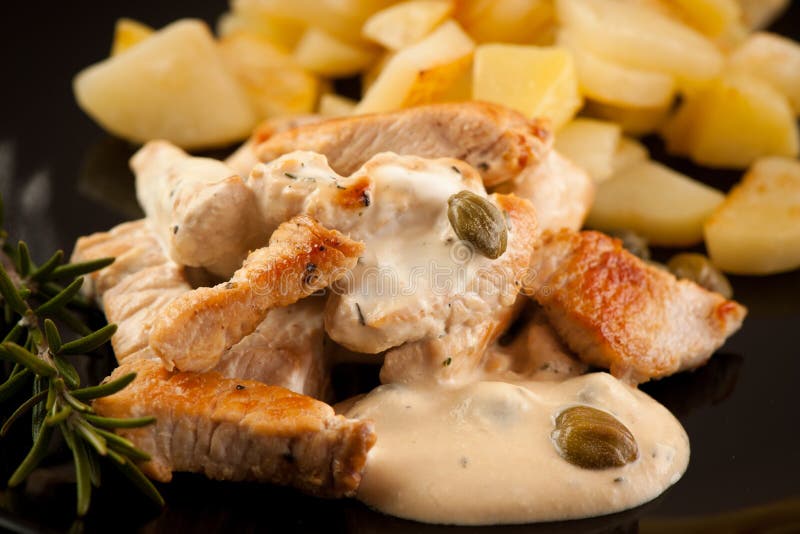 Grilled turkey meat with cheese sauce and capers on black plate