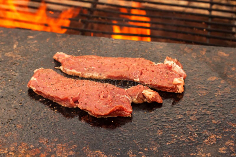 Griller le bifteck de boeuf d'un plat de granit Préparation de viande sur un feu extérieur Barbecue d'été photo libre de droits Griller le bifteck de boeuf d'un plat de granit Préparation de viande sur un feu extérieur Barbecue d'été photo libre de droits