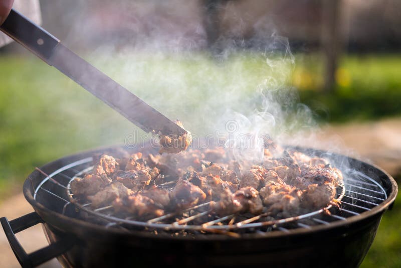 Grilling barbeque meet on the grill outdoors in the back yard. Summer time picnic. Roasting meat on metal grid on hot coals. Smoke