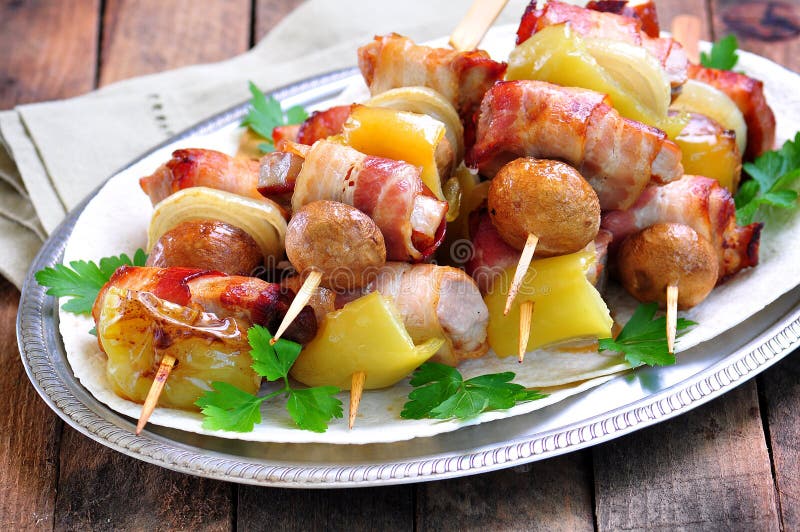 Griskött som slås in i bacon på steknålar som grillas med lökar, champinjoner och peppar arkivfoto Griskött som slås in i bacon på steknålar som grillas med lökar, champinjoner och peppar arkivfoto