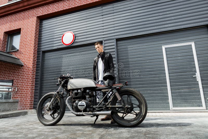 Grober Mann nahe seinem Caférennläufer-Gewohnheitsmotorrad lizenzfreie stockbilder Grober Mann nahe seinem Caférennläufer-Gewohnheitsmotorrad lizenzfreie stockbilder